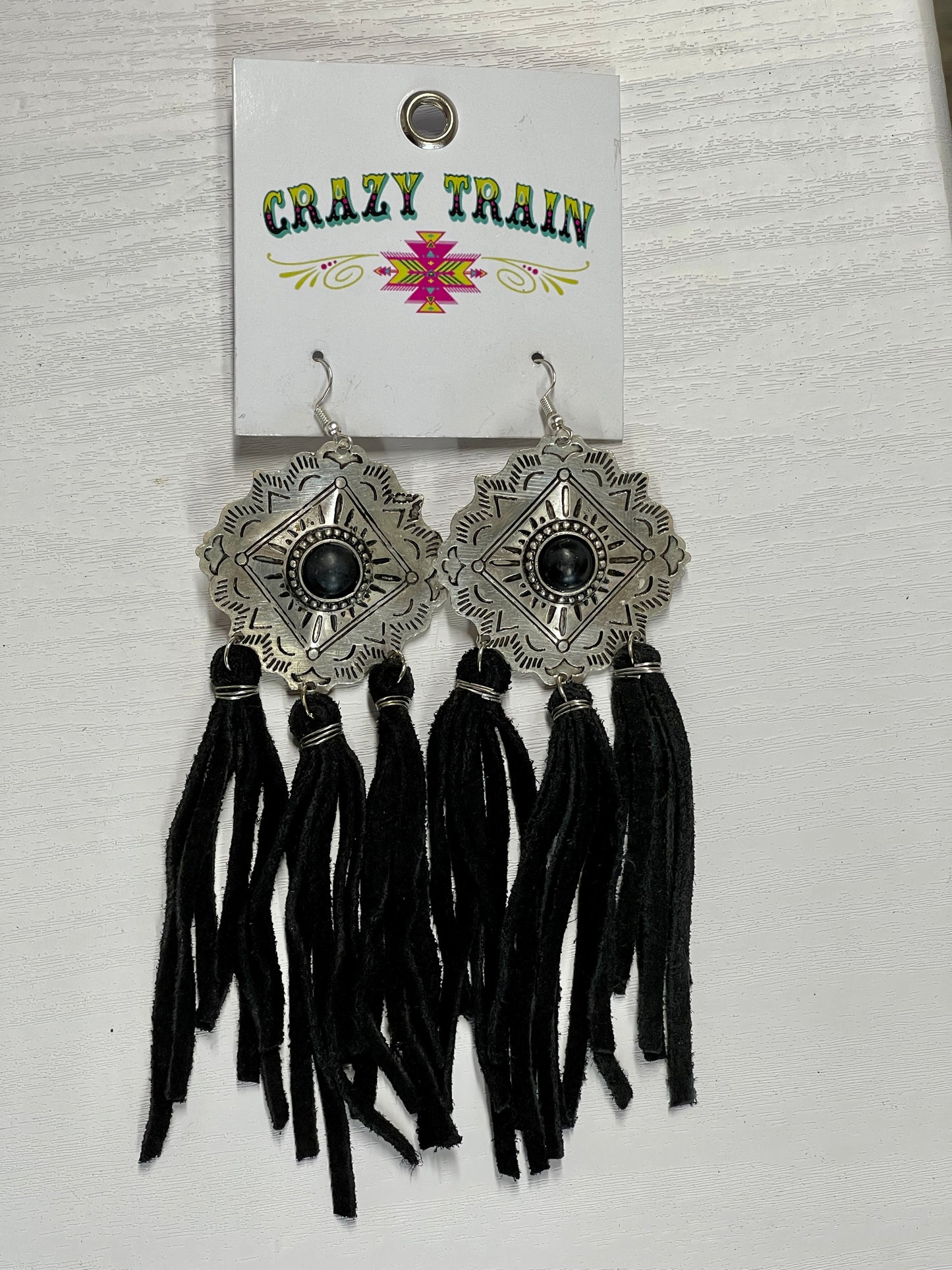 Crazy Train brand earrings. Etched silver metal diamond shaped medallions with black bead in center. 3 groups of tassels hang on the bottom. Tassels made of black leather.