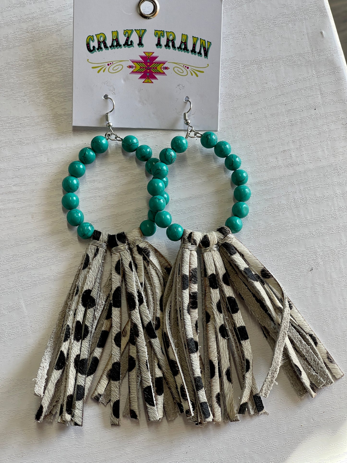 Crazy Train brand earrings. Oval shape lined with teal beads. Brown and cream cowhide printed leather tassels hang off bottom.
