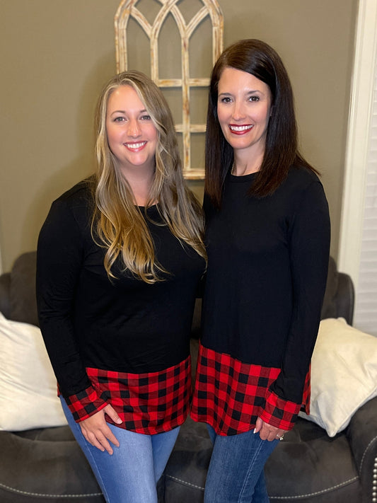2 women wearing matching shirts.  Shirt is black long sleeved with red and black plaid around the bottom of the shirt and ends of sleeves.