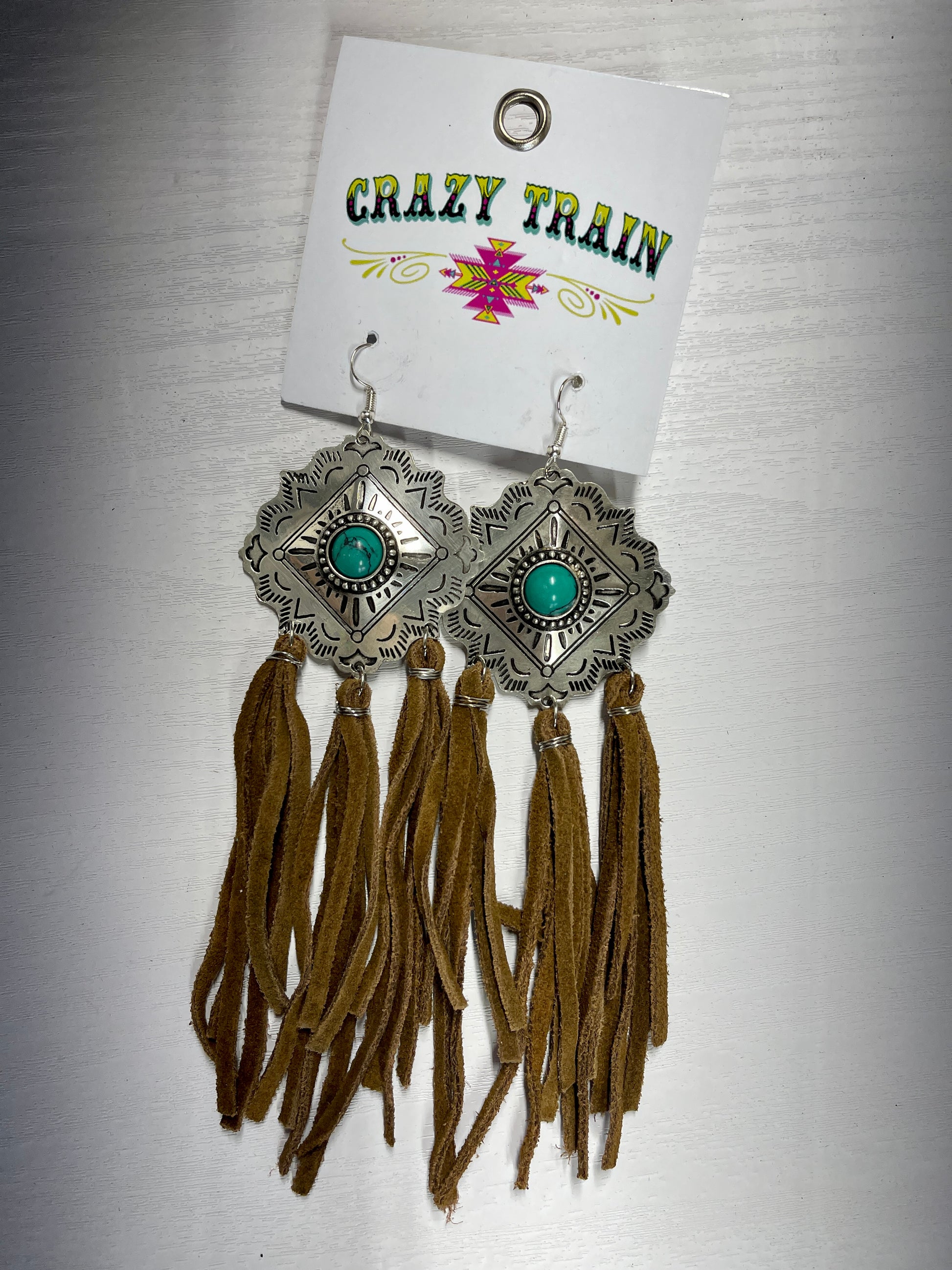 Crazy Train brand earrings. Etched silver metal diamond shaped medallions with turquoise bead in center.  3 groups of tassels hang on the bottom.  Tassels made of brown leather.