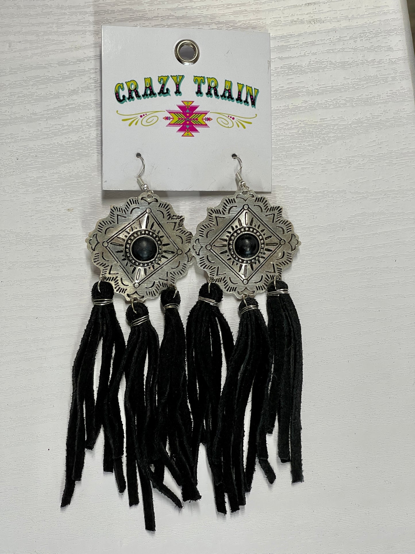 Crazy Train brand earrings. Etched silver metal diamond shaped medallions with black bead in center.  3 groups of tassels hang on the bottom.  Tassels made of black leather.