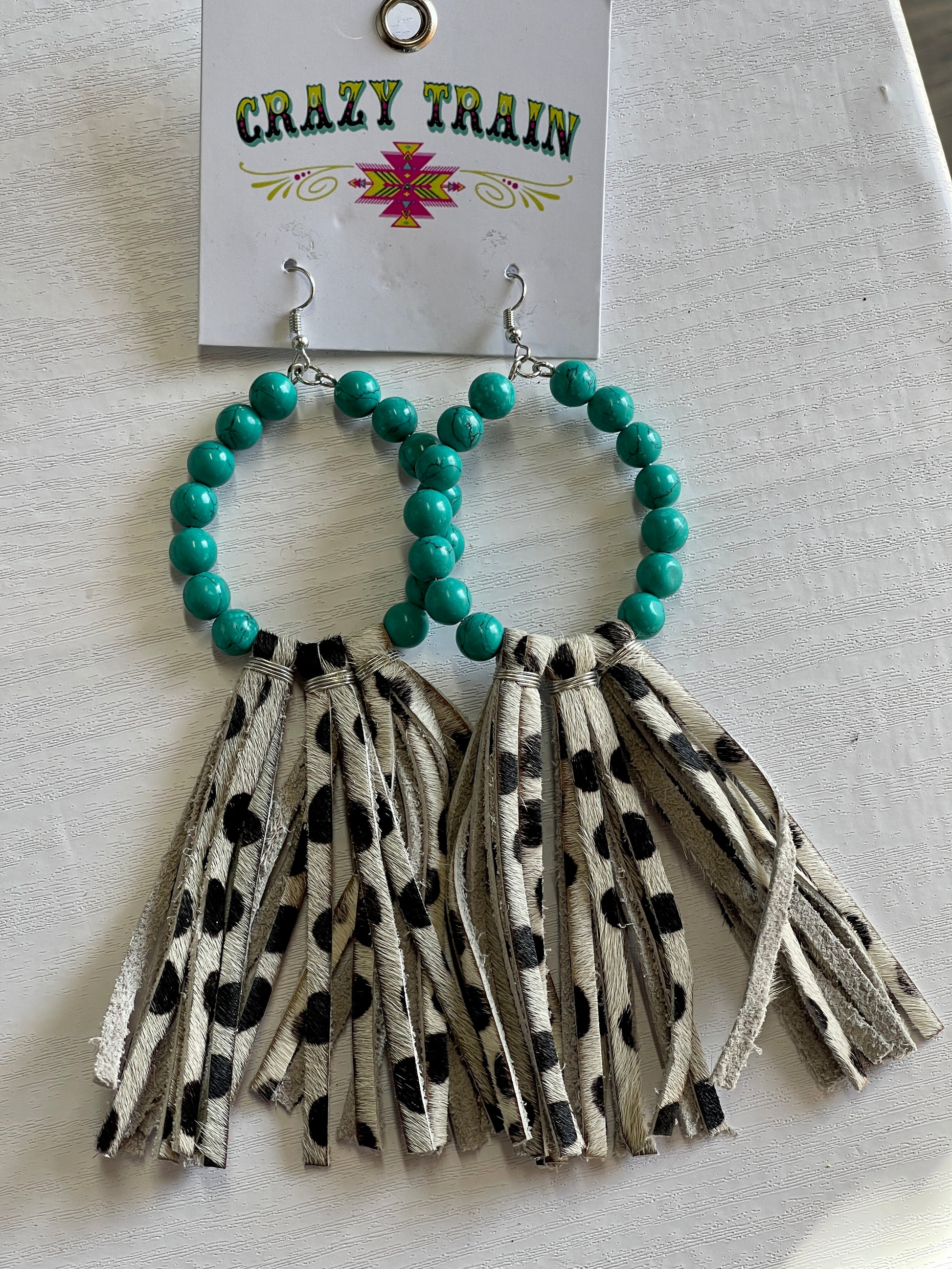 Crazy Train brand earrings.  Oval shape lined with teal beads.  Brown and cream cowhide printed leather tassels hang off bottom.