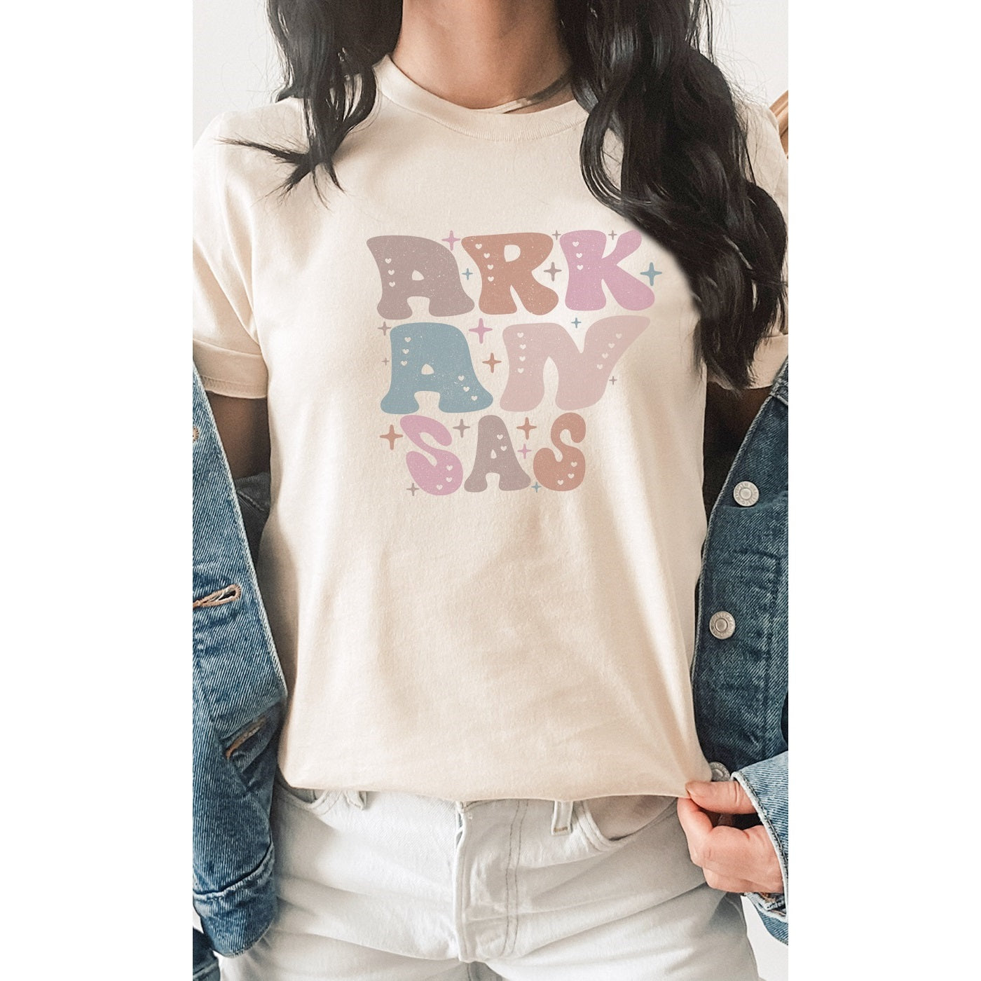 Cream colored unisex fit tee.  The word 'Arkansas' in bubble letters made out to look like the shape of the state of Arkansas. Colors of the design are light pink, dusty light blue, dusty brown, and tan made to look vintage.